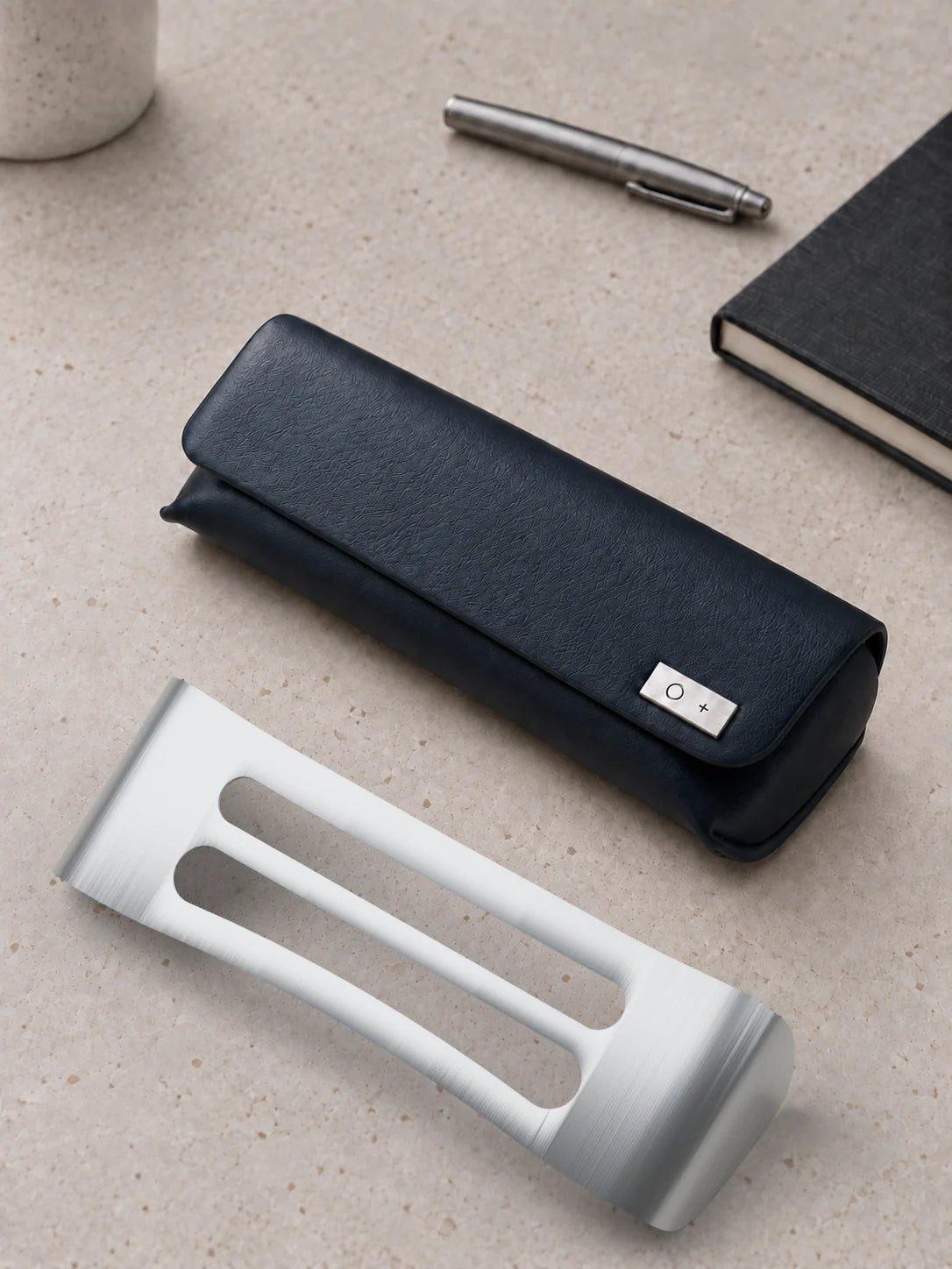 The closed navy case on a stone desk with a steel pen and a black notebook, and its bare titanium core lying in front of it.