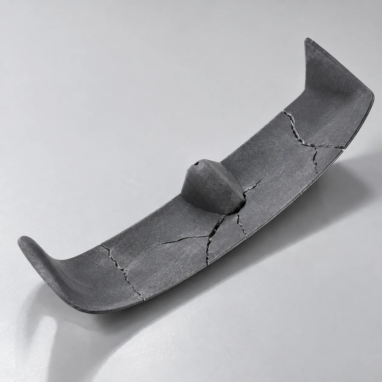 A curved dark plastic case core cracked through in several places.