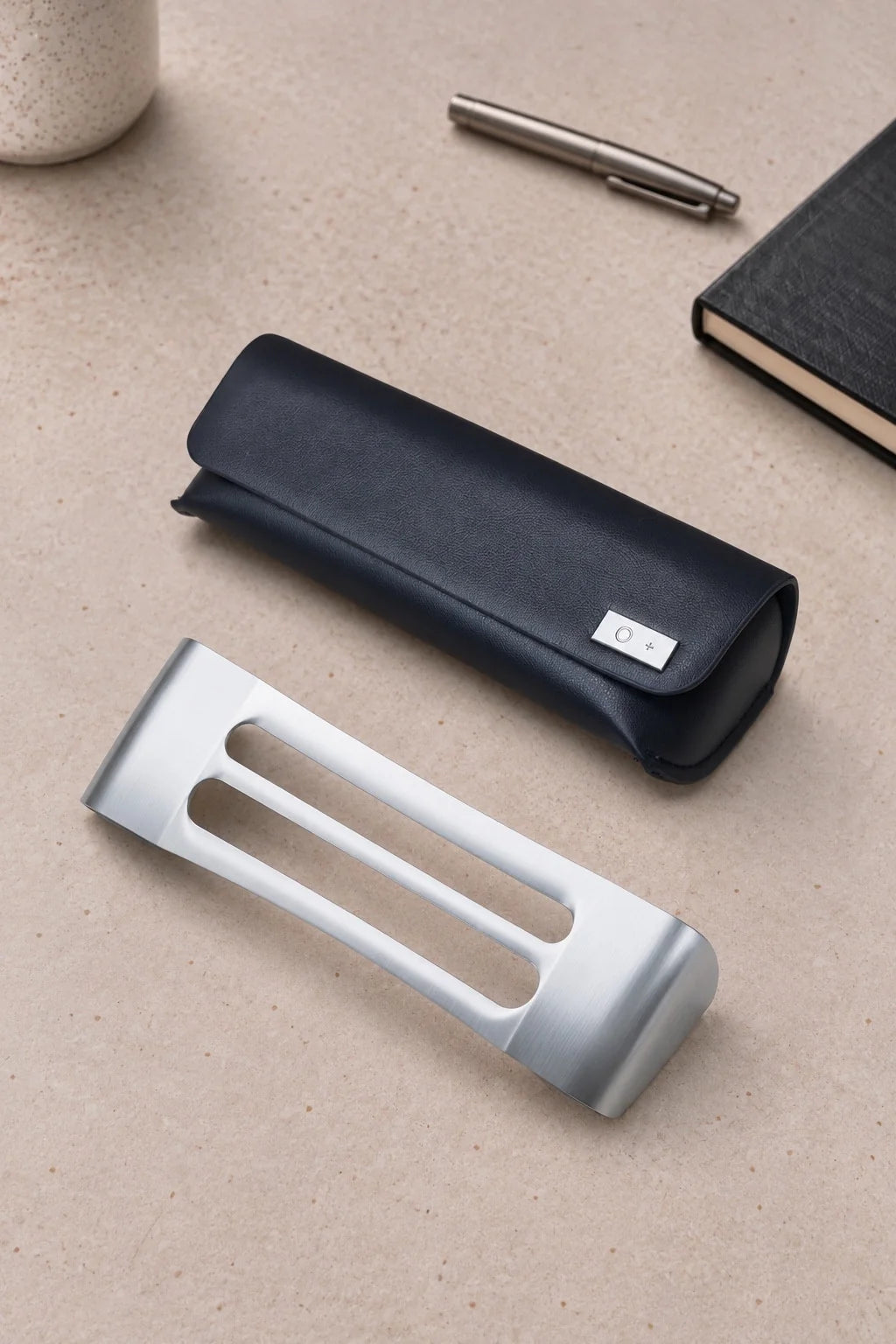 The closed navy case on a stone desk with a steel pen and a black notebook, and its bare titanium core lying in front of it.